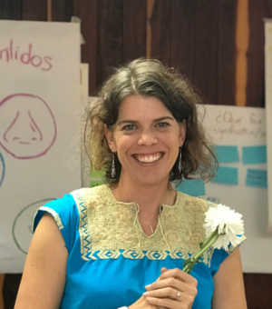 Joanna stands in front of some hand-drawn posters holding a white flower